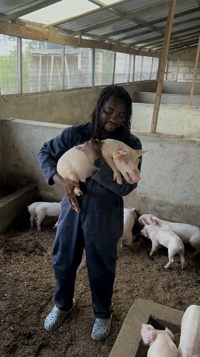 Dii-winga holding a piglet at Kihera Farms